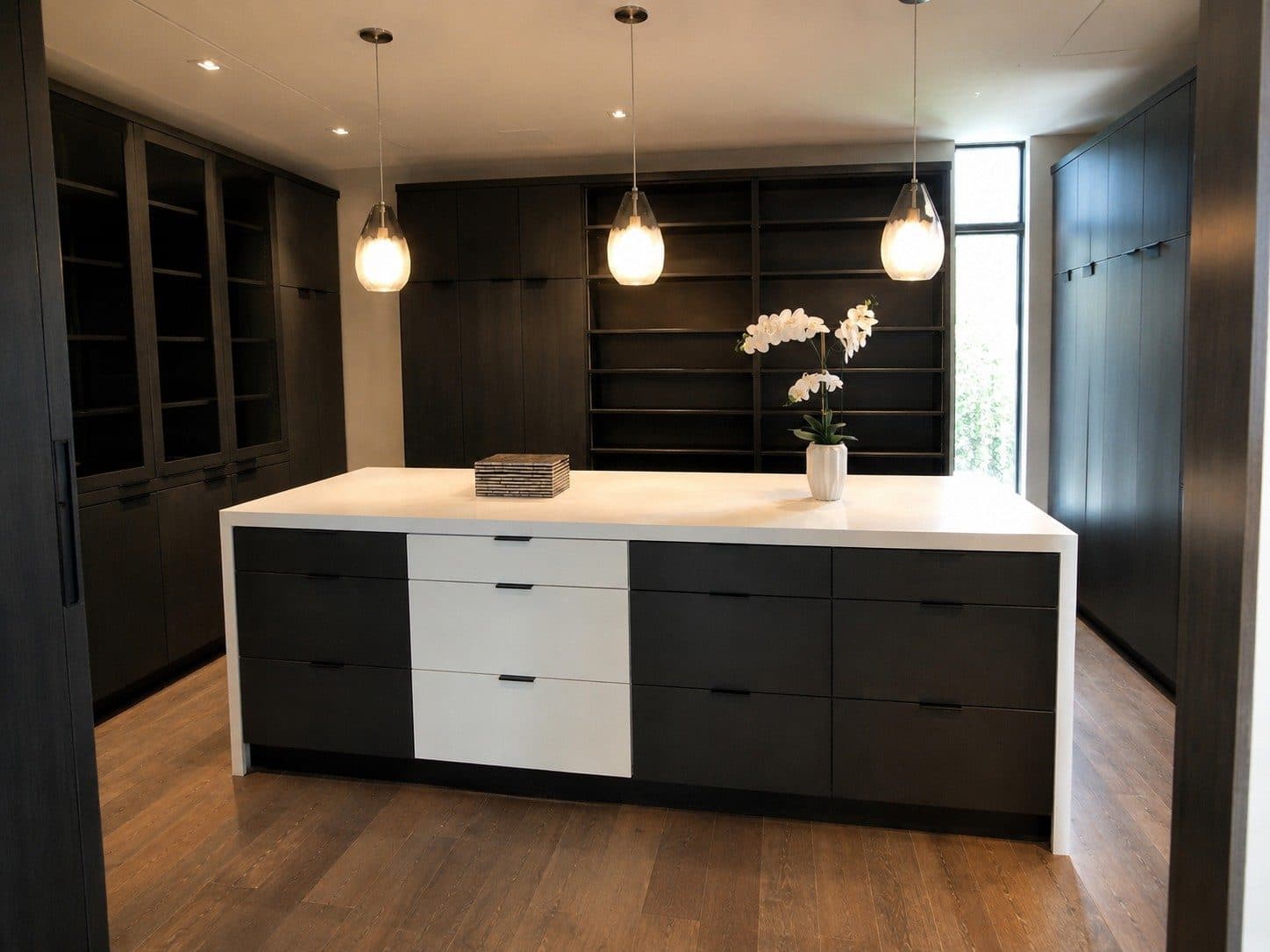 Custom dressing room with dark wardrobes, glass-front cabinets, and a white-top island